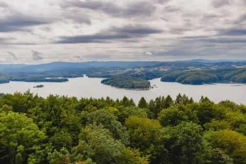 Widok na jezioro solińskie otoczone zielonymi wzgórzami i lasami pod pochmurnym niebem.