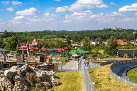 Kolorowy zamek i karuzela w **Ogrodzieńcu park rozrywki**. Dzieci bawią się na zjeżdżalni i placu zabaw.