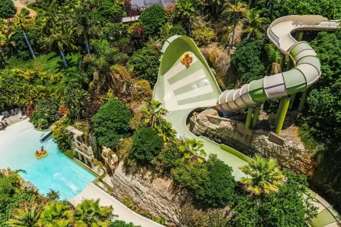 Ekscytująca zjeżdżalnia w Siam Park, z osobą na pontonie wpadającą do basenu. Wokół bujna roślinność.