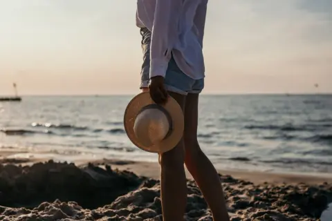 Spacer po plaży w Kołobrzegu. Słońce zachodzi nad morzem, a w dłoni trzymam słomkowy kapelusz.