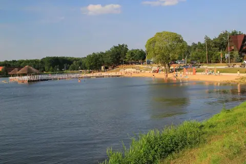 Słoneczny dzień nad zalewem Siemiatycze. Ludzie odpoczywają na piaszczystej plaży, niektórzy kąpią się w wodzie.