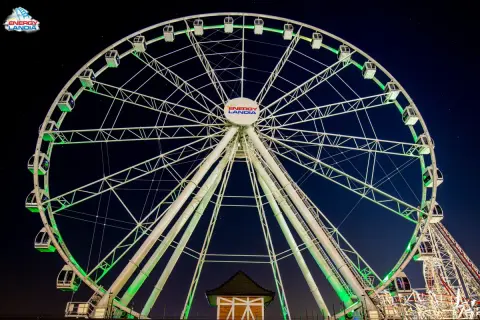 Ogromny diabelski młyn Energylandia lśni zielonym światłem na tle nocnego nieba.