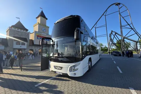 Biały autokar czeka na pasażerów przed wejściem do Energylandii. W tle widać zamek i kolejkę górską. To idealny pociąg do Energylandii!