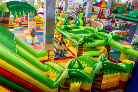 Kolorowy park rozrywki we Wrocławiu z dmuchanymi zjeżdżalniami i palmami. Dzieci biegają po kolorowej macie.