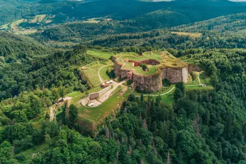 Forteca na wzgórzu, otoczona lasem, niczym srebrna góra w zieleni.