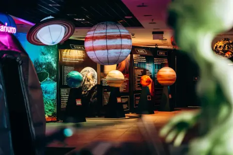 Modele planet i pierścieni Saturna w kosmo parku. W tle tablice informacyjne o Ziemi, Marsie i Jowiszu.