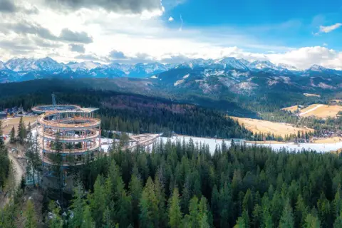 Drewniana konstrukcja sky walk w Poroninie wznosi się nad lasem, oferując widok na ośnieżone Tatry.