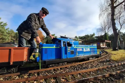 Mężczyzna w czapce i kurtce obsługuje niebieską lokomotywę PKP SM42, która jest częścią kolejki. Obok wagon towarowy.