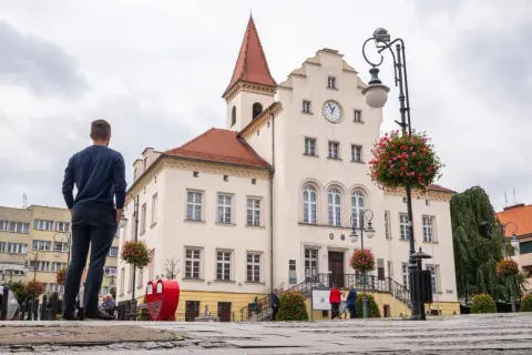 Mężczyzna patrzy na ratusz w Trzebnicy, jedno z głównych atrakcji miasta. W tle widać zegar i czerwone serca.