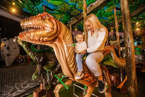 Uśmiechnięta mama z dzieckiem na dinozaurze w góraszka park rozrywki. Wesoła przejażdżka wśród prehistorycznych stworzeń.