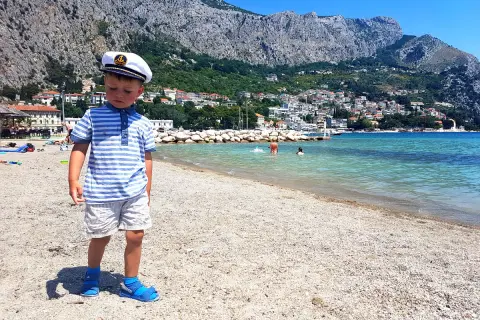 Chłopiec w kapitańskim kapeluszu na plaży w Chorwacji. W tle góry i miasteczko. Idealne miejsce na wakacje, jak w parku rozrywki Chorwacja.
