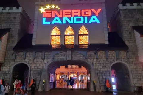 Wejście do Energylandii nocą, mimo deszczu, widać ludzi wchodzących pod łukiem.