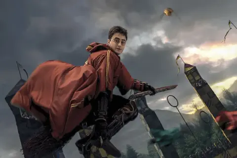 Harry Potter na miotle, w czerwonym szacie, ściga Złoty Znicz podczas meczu quidditcha. To scena z filmu "Harry Potter i Zakazana Podróż".