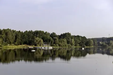 Spokojne jezioro Przeczyckie z odbijającymi się w wodzie drzewami i żaglówkami. Na wodzie widać samotną łódkę.