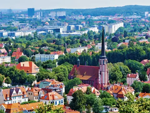 Widok z punkt widokowy Gdańsk: czerwona ceglana katedra z wysoką wieżą, otoczona zielenią i dachami domów. W tle nowoczesne budynki.