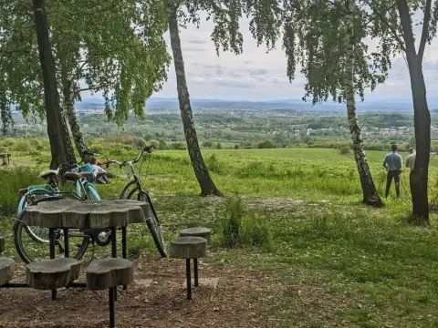Idealny punkt widokowy Kraków. Dwa rowery, drewniany stolik i ławki czekają na turystów. W oddali rozciąga się malowniczy krajobraz.