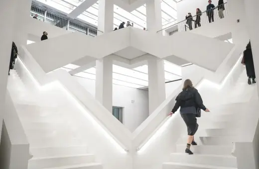 W nowoczesnym, białym wnętrzu nowego muzeum w Warszawie, ludzie wchodzą po schodach.