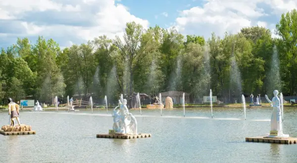 Park mitologii na wodzie z rzeźbami bogów i bogiń, otoczony zielenią i fontannami.