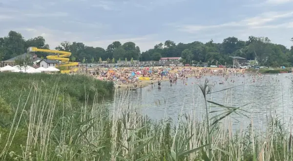 Tłum ludzi wypoczywa nad wodą na plaży w Lisowicach. W oddali widać żółtą zjeżdżalnię wodną.