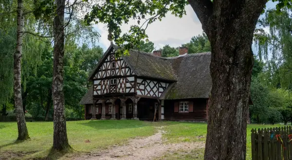 Drewniany dom z muru pruskiego i strzechą, otoczony zielenią. Jedna z atrakcji Olsztynka, zapraszająca do podróży w czasie.