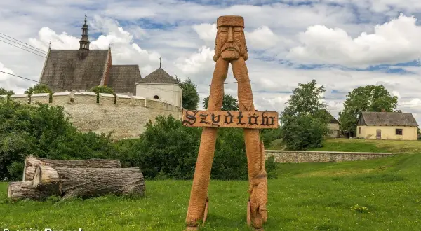 Drewniana rzeźba wita w Szydłowie, jednej z pięknych świętokrzyskich atrakcji. W tle zamek i malownicze zabudowania.
