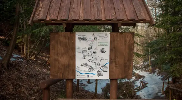 Mapa szlaku turystycznego w rezerwacie przyrody Nieożywionej Skamieniałe Miasto w Ciężkowicach. Drewniana tablica informacyjna w lesie.