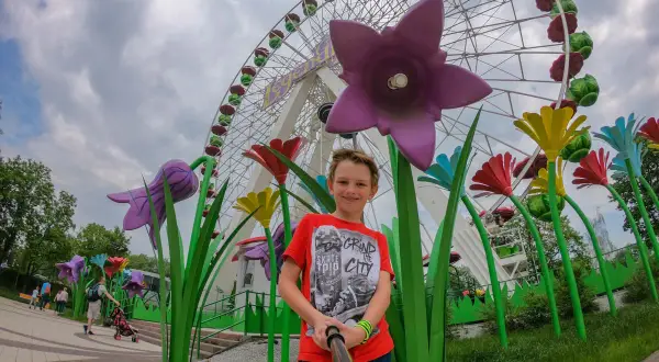 Chłopiec pozuje do selfie na tle diabelskiego młyna w chorzowskim wesołym miasteczku, otoczony kolorowymi, gigantycznymi kwiatami.
