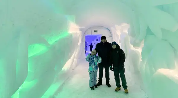 Rodzina w lodowym tunelu, gdzieś w okolicy wioski Mikołaja w Finlandii. Ściany lśnią zielonym światłem.