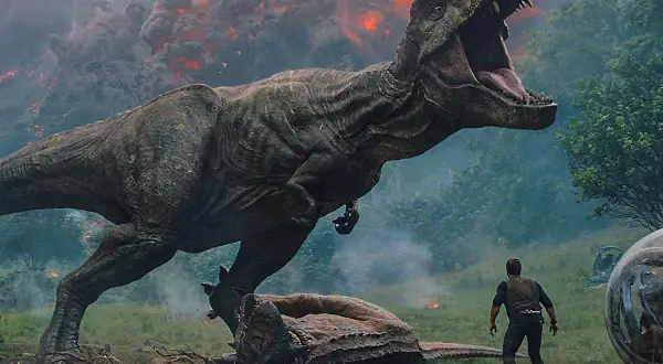 Tyranozaur atakuje w parku rozrywki Jurassic World, człowiek stoi w obliczu chaosu, w tle wulkaniczna erupcja.