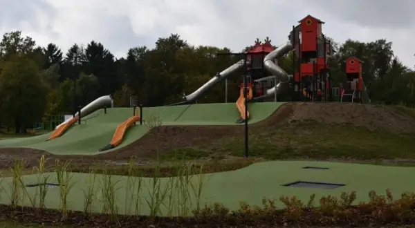 Nowoczesny lunapark w Łodzi z wieloma zjeżdżalniami, wieżami i trampolinami wbudowanymi w zielone wzgórza.
