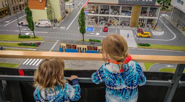 Dwie dziewczynki oglądają miniaturową ulicę z tramwajem i budynkami w parku miniatur Wrocław.