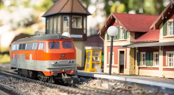 Miniaturowy pociąg na torach w parku miniatur i kolejek dziwnów. Stacja z budynkiem i budką telefoniczną.