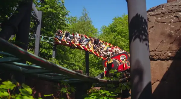 Pasażerowie na kolejce górskiej w kopenhaga park rozrywki, jadący przez zielony las.