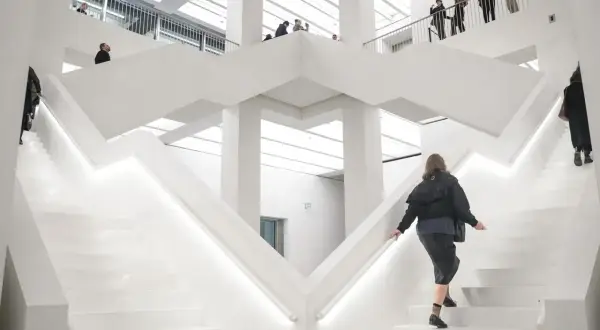 W nowoczesnym, białym wnętrzu nowego muzeum w Warszawie, ludzie wchodzą po schodach.
