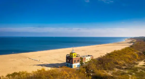 Gdańsk plaża z charakterystycznym budynkiem i piaszczystym wybrzeżem. Błękitne morze i niebo tworzą spokojny krajobraz.
