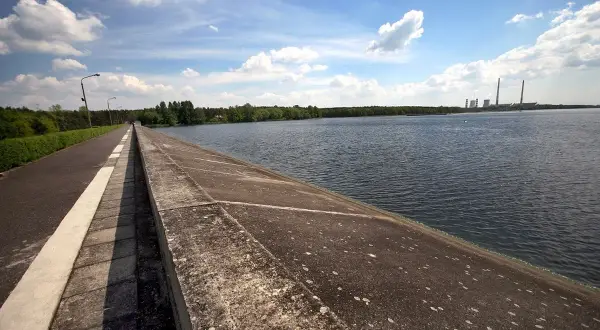 Droga biegnie wzdłuż betonowego muru nad spokojnym zalewem rybnickim. W oddali widać elektrownię.