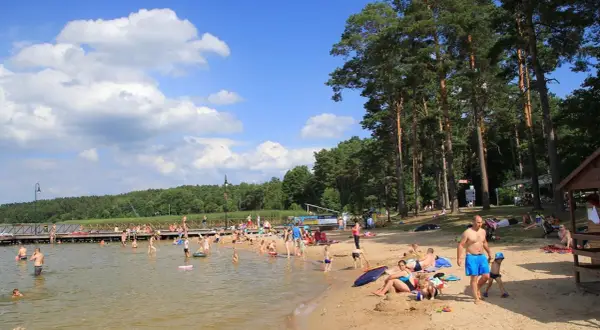 Słoneczna augustowska plaża tętni życiem. Ludzie kąpią się, opalają i relaksują na piasku, ciesząc się letnim dniem nad jeziorem.