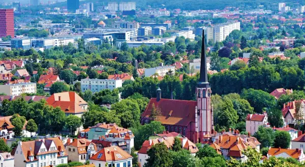 Widok z punkt widokowy Gdańsk: czerwona ceglana katedra z wysoką wieżą, otoczona zielenią i dachami domów. W tle nowoczesne budynki.