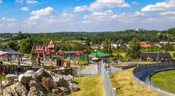 Kolorowy zamek i karuzela w **Ogrodzieńcu park rozrywki**. Dzieci bawią się na zjeżdżalni i placu zabaw.
