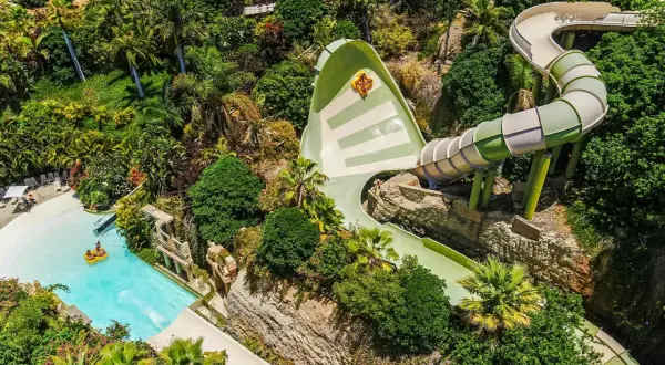 Ekscytująca zjeżdżalnia w Siam Park, z osobą na pontonie wpadającą do basenu. Wokół bujna roślinność.