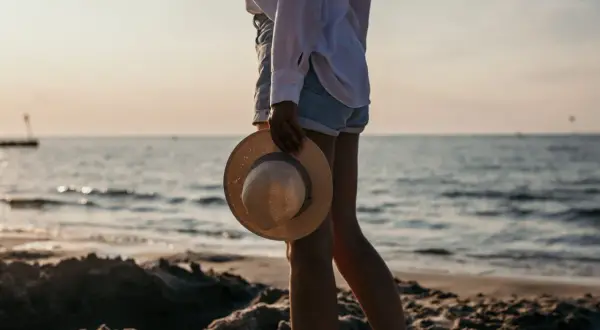 Spacer po plaży w Kołobrzegu. Słońce zachodzi nad morzem, a w dłoni trzymam słomkowy kapelusz.
