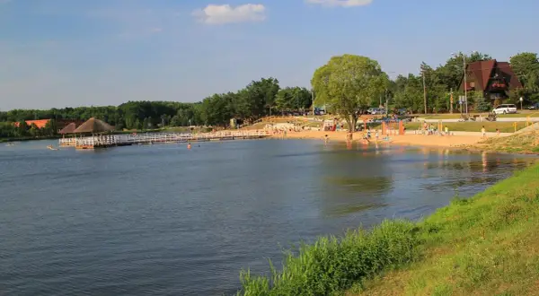 Słoneczny dzień nad zalewem Siemiatycze. Ludzie odpoczywają na piaszczystej plaży, niektórzy kąpią się w wodzie.