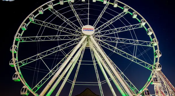 Ogromny diabelski młyn Energylandia lśni zielonym światłem na tle nocnego nieba.