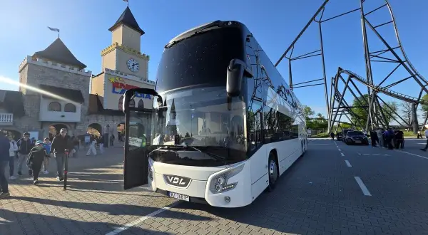 Biały autokar czeka na pasażerów przed wejściem do Energylandii. W tle widać zamek i kolejkę górską. To idealny pociąg do Energylandii!