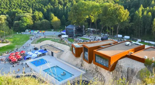 Ulinapark tętni życiem: koncert na scenie, baseny, punkty gastronomiczne i nowoczesne budynki na skale.