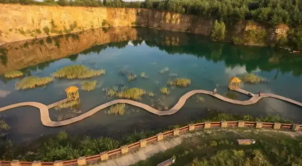 Malowniczy park Gródek z drewnianymi kładkami wijącymi się pośród turkusowej wody i wysepek z trzcinami.