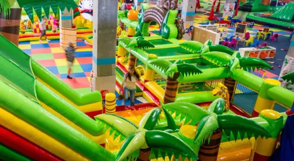 Kolorowy park rozrywki we Wrocławiu z dmuchanymi zjeżdżalniami i palmami. Dzieci biegają po kolorowej macie.