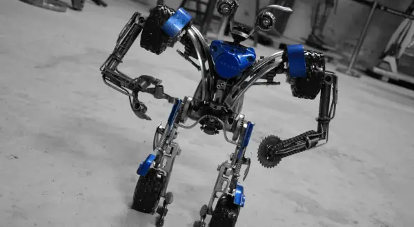 Robot z muzeum robotów Moszna, wykonany z metalowych części i ozdobiony niebieskimi akcentami, stoi na betonowej posadzce.
