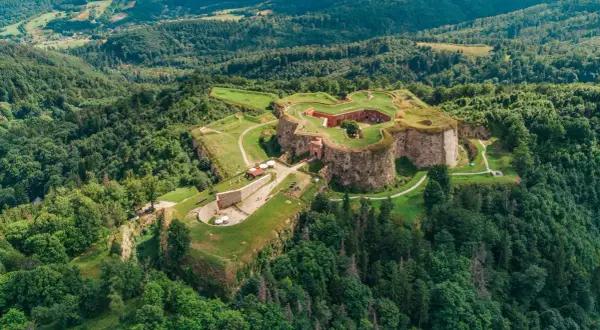 Forteca na wzgórzu, otoczona lasem, niczym srebrna góra w zieleni.