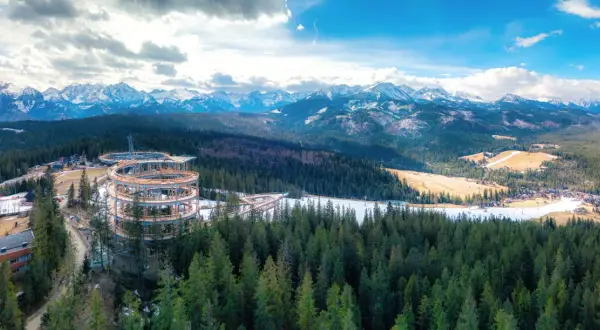 Drewniana konstrukcja sky walk w Poroninie wznosi się nad lasem, oferując widok na ośnieżone Tatry.